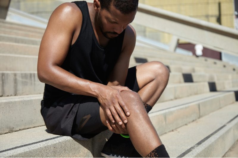 a male athlete sits on steps, holding injured knee