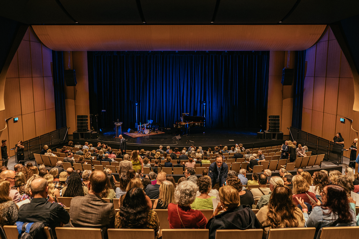 View of the Desautels Concert Hall stage from the upper back of the hall with audience members in their seats.