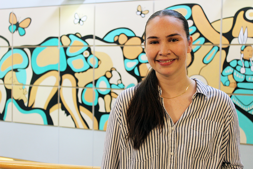 Justice Spence stands in the College of Nursing atrium with a colourful mural behind her.