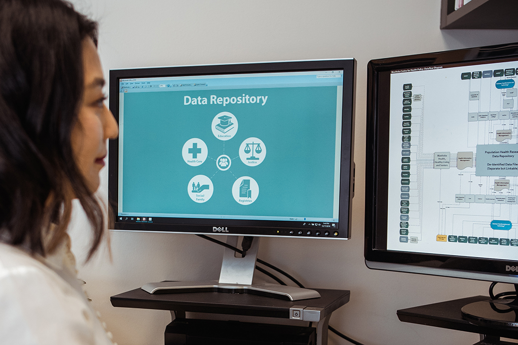 A woman looks at two computer screens containing information about the Manitoba Population Research Data Repository.