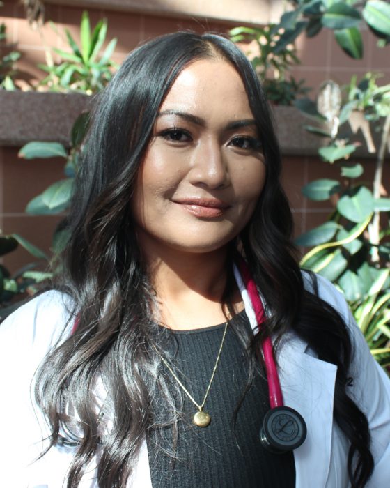 Portrait of Kimberly Dela Rosa. She is wearing a white coat and a stethoscope. 