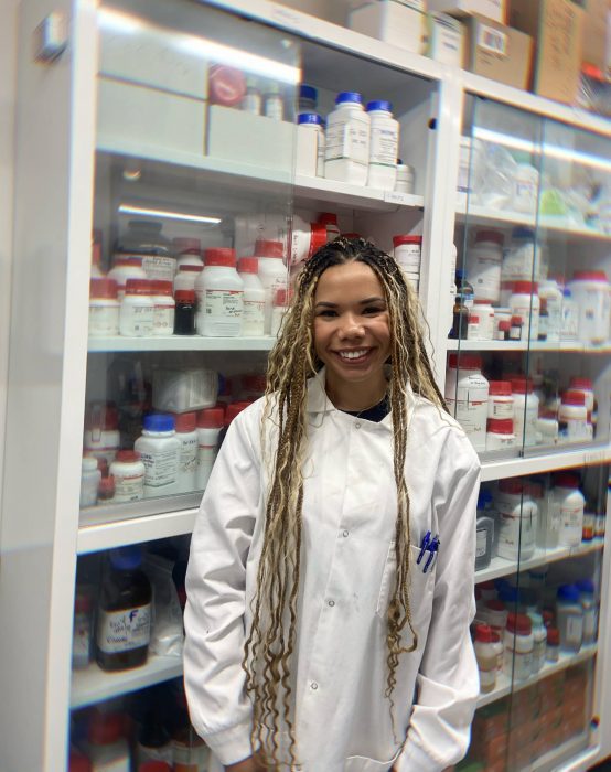 person in lab coat standing by pharmaceuticals 