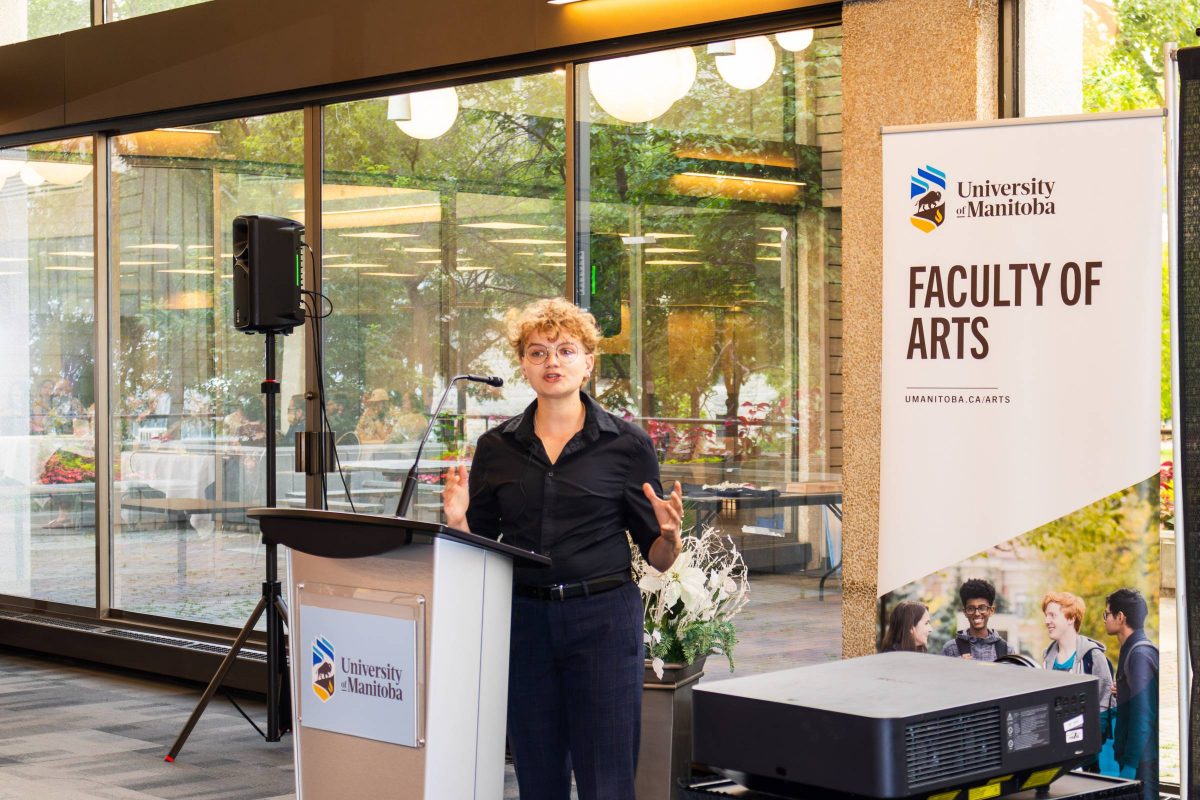 Female speaker standing behind a podium with arms raised, speaking to the audience.