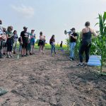 People listen to a lecture in front of planted field