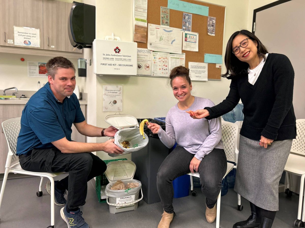 Three colleagues demonstrate the composting system in their office lunchroom.