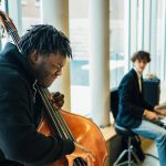 One person on the left playing a double bass, with one on the right playing the drums