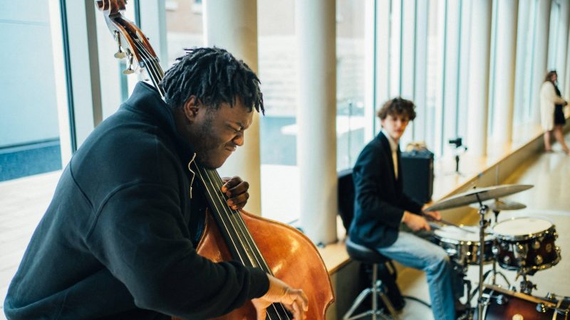 One person on the left playing a double bass, with one on the right playing the drums