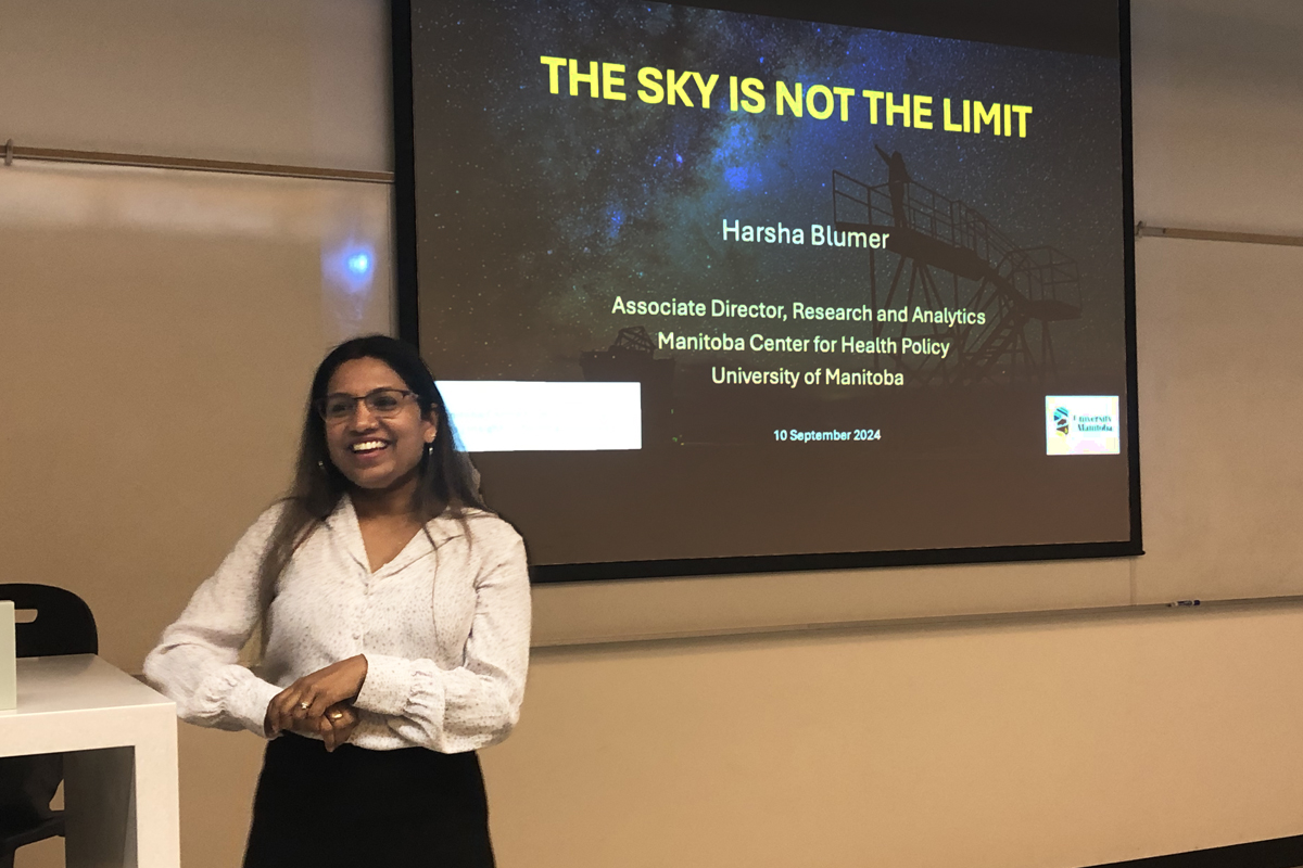 Dr. Harsha Blumer, giving a presentation with a screen behind her