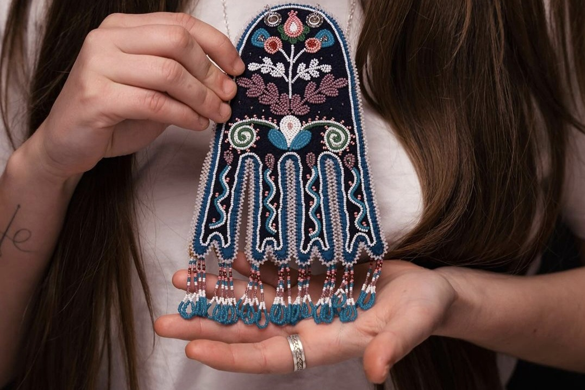 Woman with brown hair holds a beaded artwork.