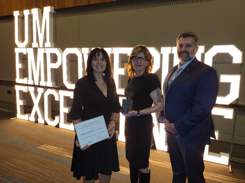 Photo of three people standing before UM Empowering Excellence sign