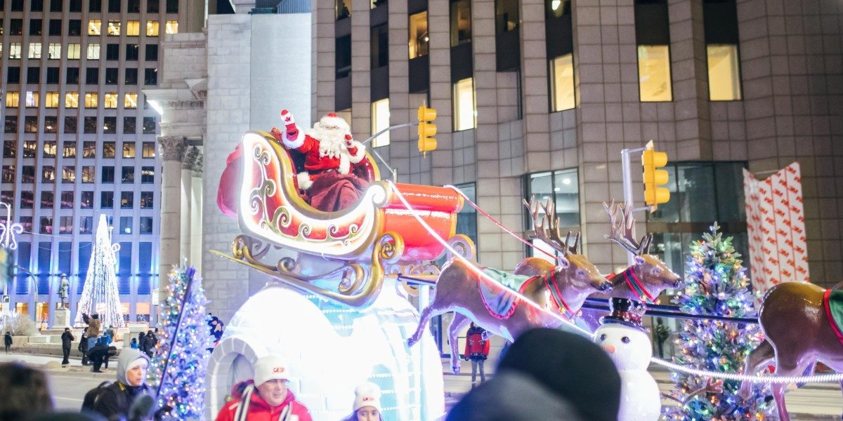 Santa Claus in a sleigh pulled by reindeer. In the background, trees bedecked with Christmas lights and skyscrapers.