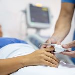 A nurse places a pulse oximeter on a patient laying in a hospital bed.