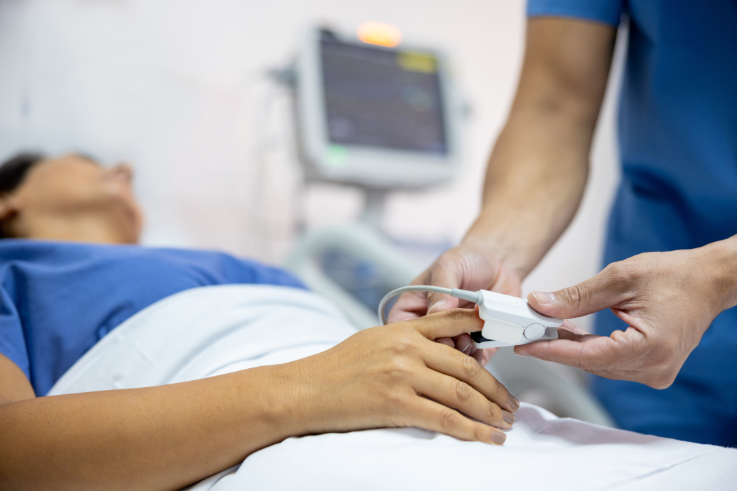 A nurse places a pulse oximeter on a patient laying in a hospital bed.