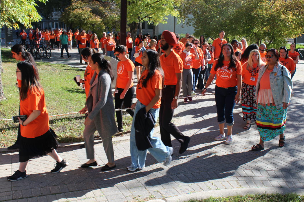 Dozens of people wearing orange shirts walk at the Fort Garry campus.