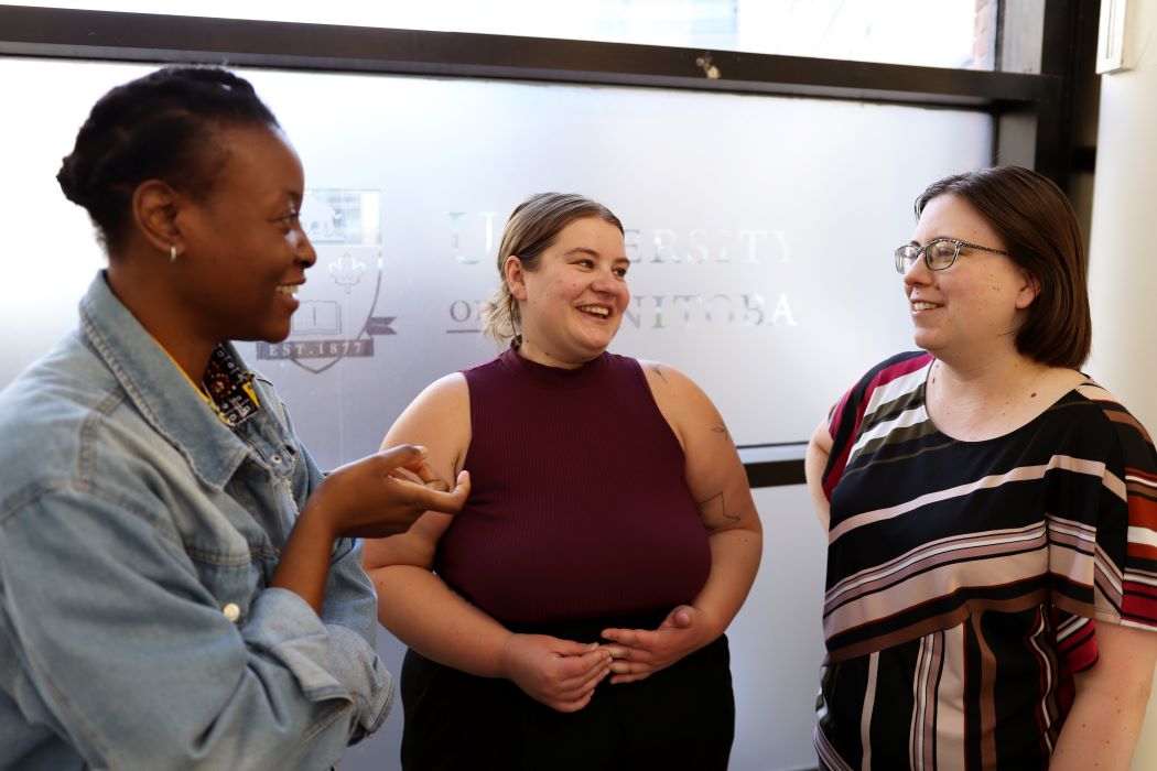 Three women stand in a semi-circle having a conversation.