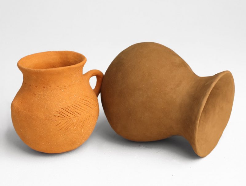 Two ceramic vessels created by MFA student Netsanet Shawl using locally sourced clay, featuring natural textures and earthy tones; one vessel has a handle and engraved leaf pattern.