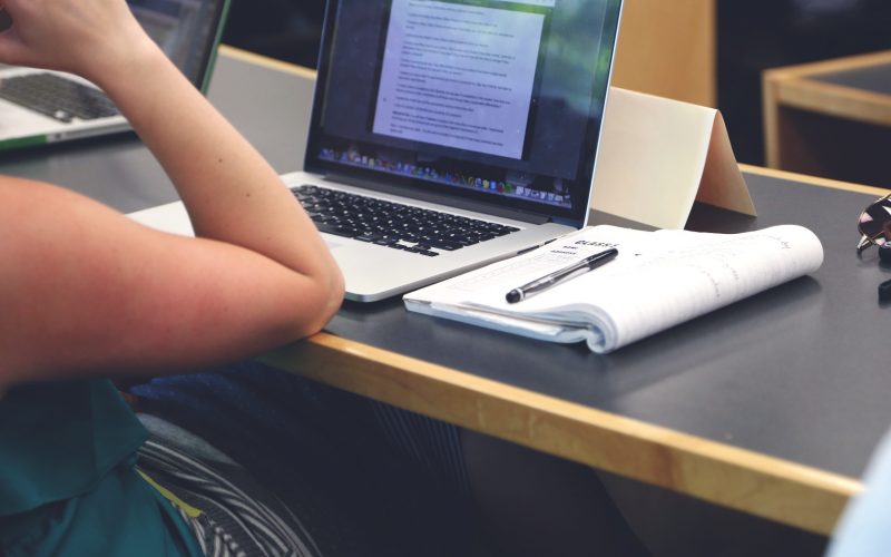 person resting arm on desk with open laptop and notebook