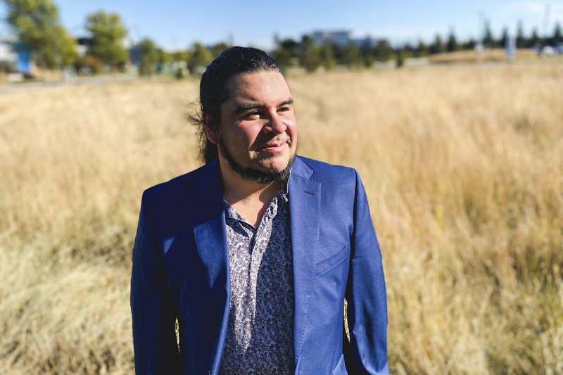 Kyle Bobiwash stands in a field, wearing a blue suit and looking off to the side