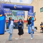 Three student volunteers greet new students at orientation. They stand in front of an inflatable University of Manitoba arch and hold signs that say "We are all Bisons"