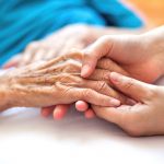 Closeup of a health-care worker's hands holding the hand of a patient.