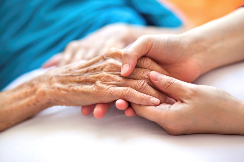 Closeup of a health-care worker's hands holding the hand of a patient.