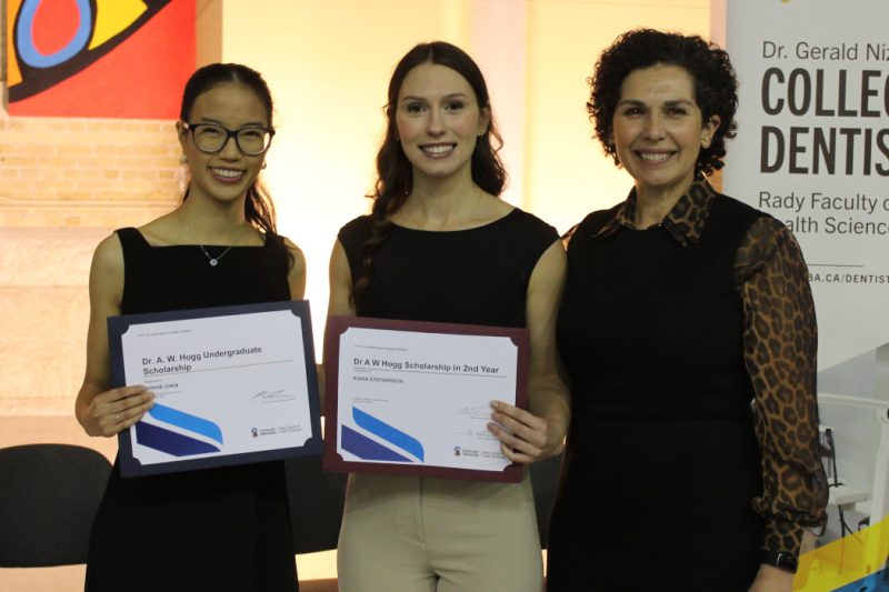 Two students and dean pose for a photo. The students are holding up award certificates. 