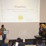 Two women on stage presenting with a projector to people at a workshop.