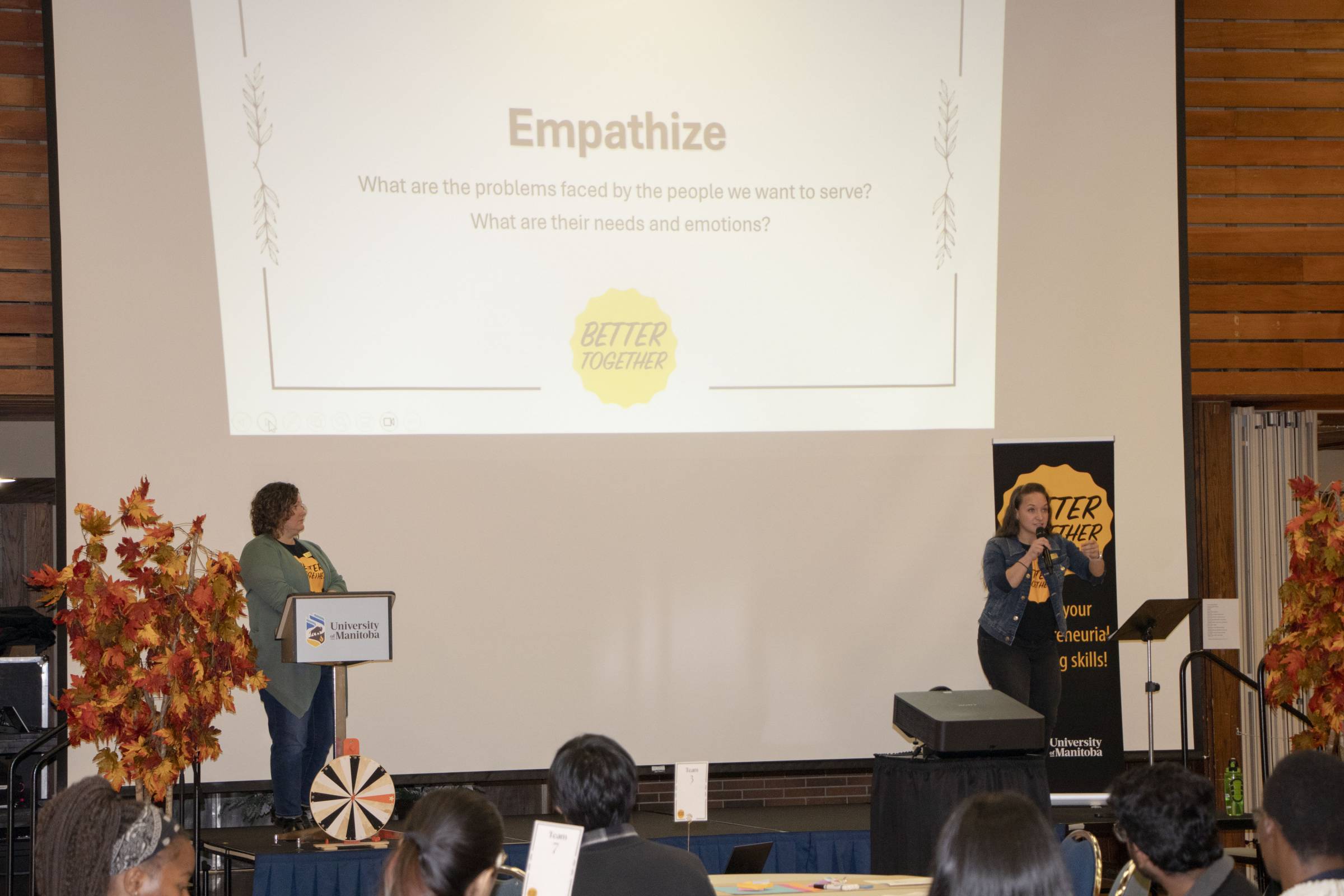 Two women on stage presenting with a projector to people at a workshop.