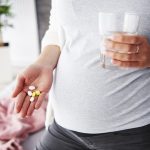 Pregnant woman with a hand outstretched, holding pills.