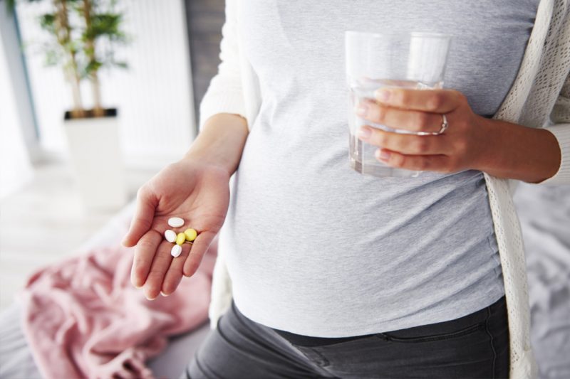 Pregnant woman with a hand outstretched, holding pills.