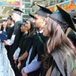 Graduands standing in the atrium at Bannatyne campus for convocation. A colourful piece of Indigenous artwork can be seen in the background encircling them.