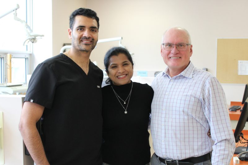 Three people pose for a photo in a dental clinic.