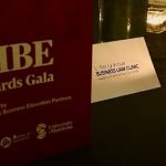 Photo of 2024 VIBE Awards Gala program on table top beside tent card of L. Kerry Vickar Business Law Clinic