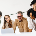 Photo of diverse professionals conferring around a laptop.