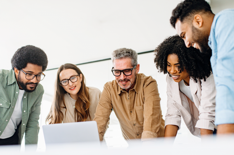 Photo of diverse professionals conferring around a laptop.