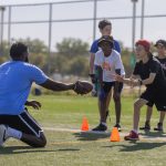 A Mini U leader passes a football to a camper