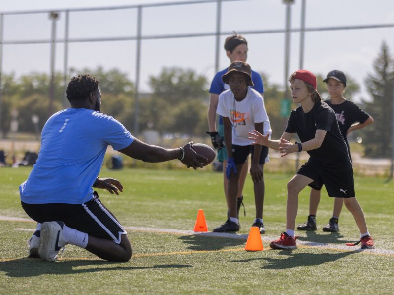 A Mini U leader passes a football to a camper