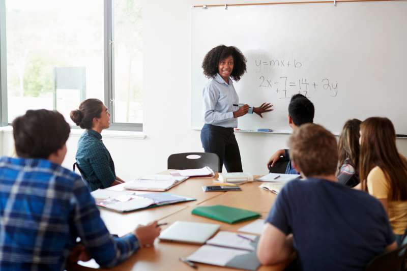 woman teaching math on whiteboard to students