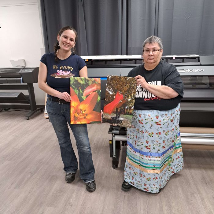 Two women holding canvases of art.