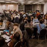 A room full of about 100 people sitting at round tables, all engaged in conversation.