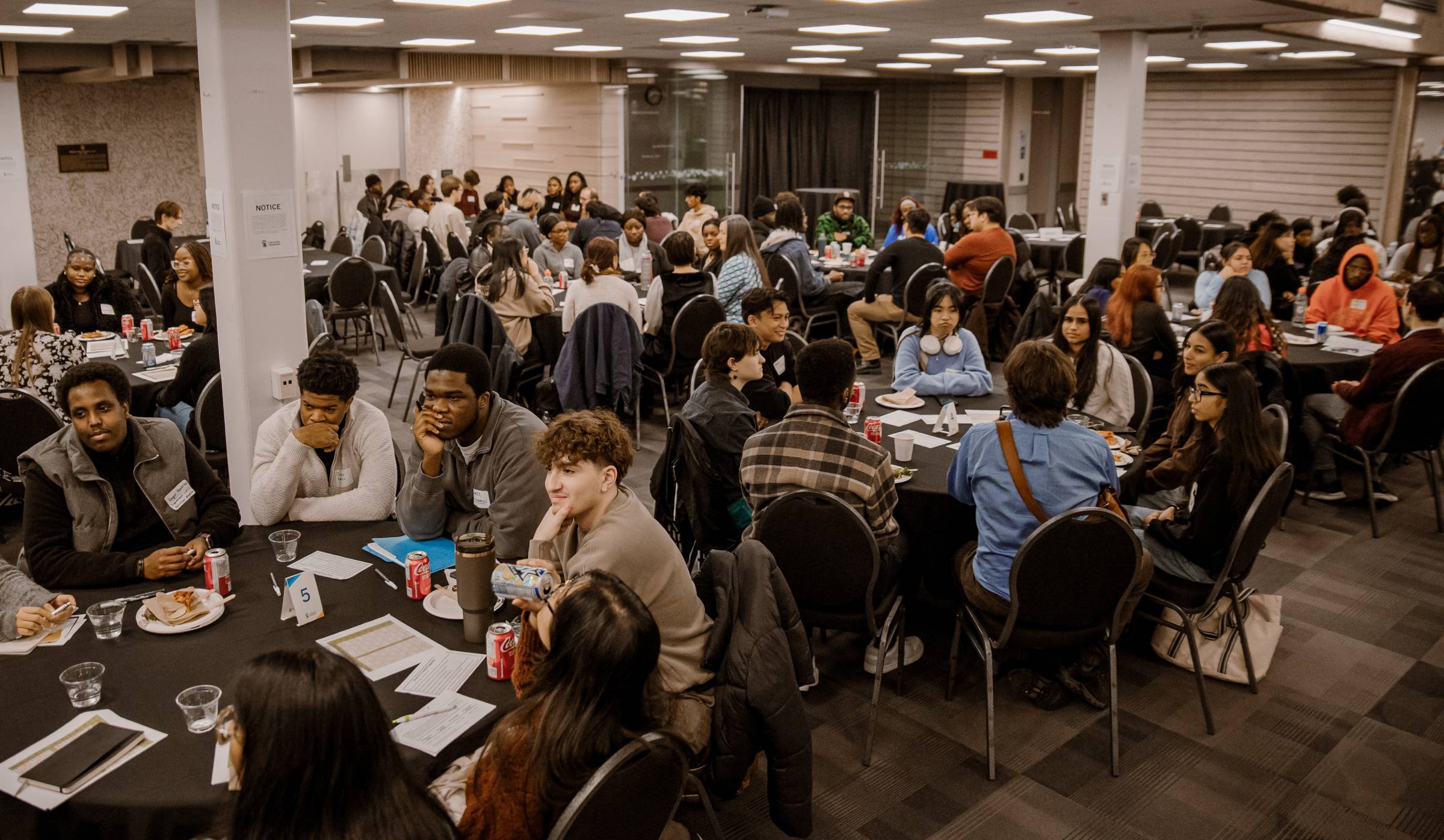 A room full of about 100 people sitting at round tables, all engaged in conversation.