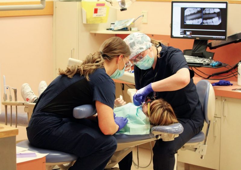 Two people at the UM dental college care for a child who is in a reclined dental chair.