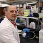 Dr. Jason Kindrachuk wearing a white lab coat in a laboratory.