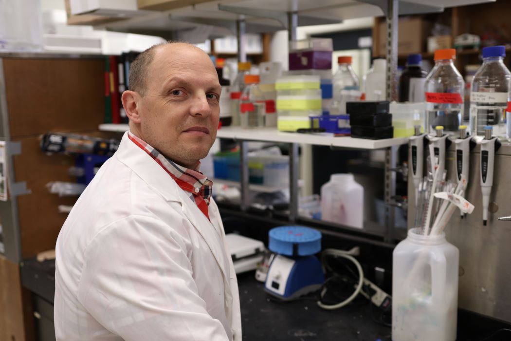 Dr. Jason Kindrachuk wearing a white lab coat in a laboratory.