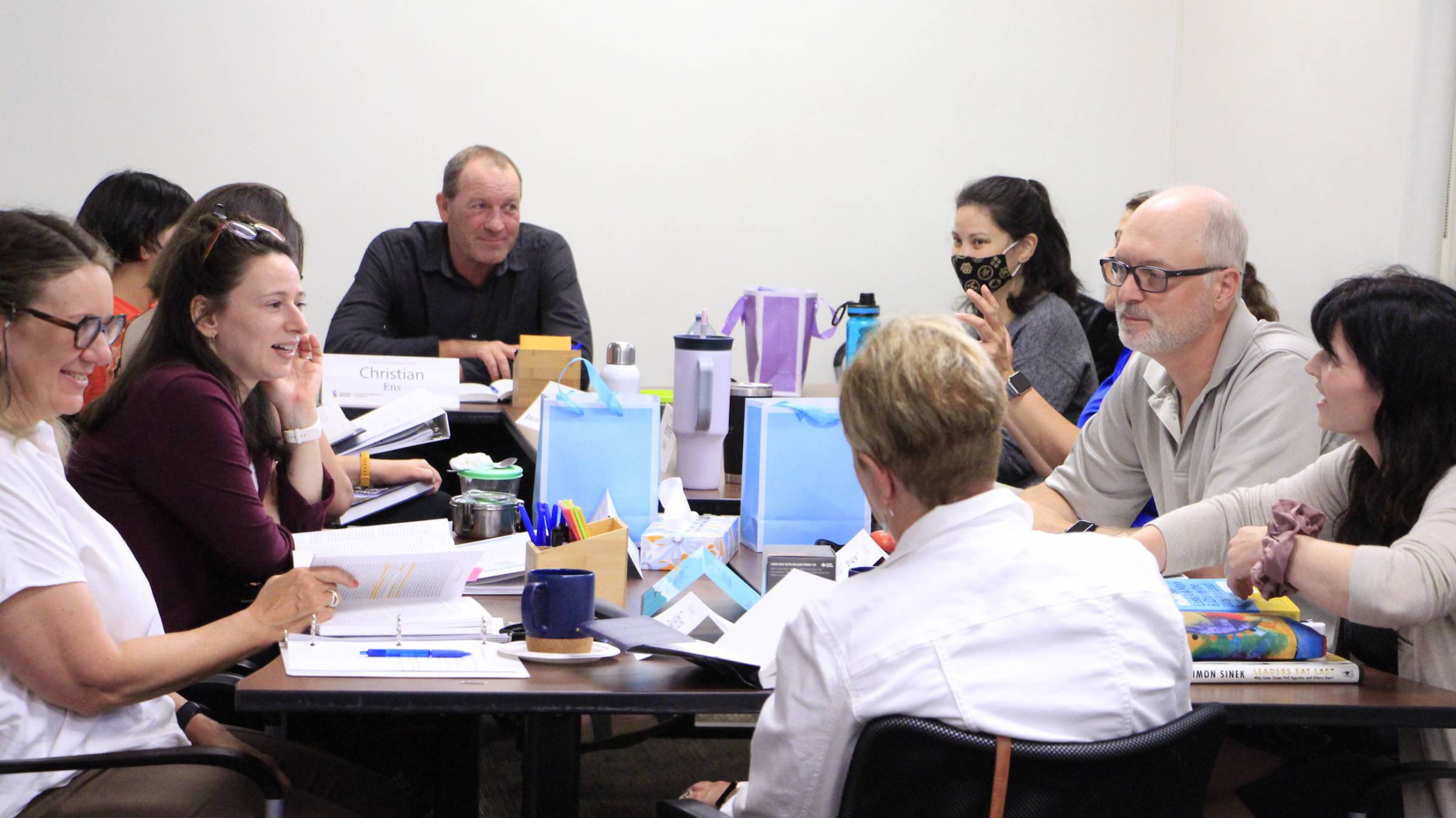 Workshop participants sit around a large table with notebooks and binders.