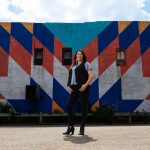 Diane Roussin stands in front of a colourful mural, looking at the camera