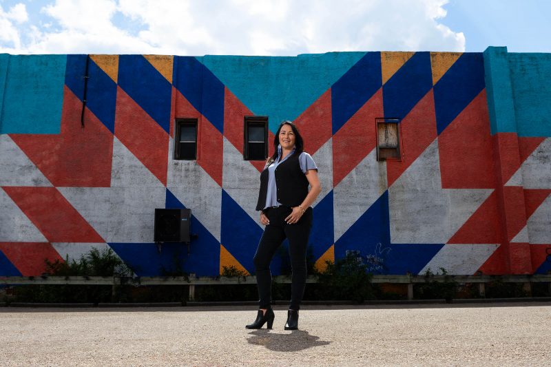 Diane Roussin stands in front of a colourful mural, looking at the camera