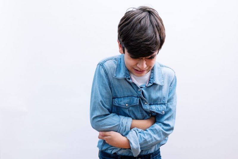 A standing boy clutches his stomach in pain.