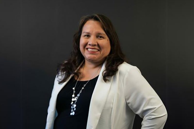 woman, wearing a white blazer and black top, with happy expression looking into the camera