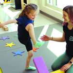 A physiotherapist works with a young child in a colourful environment.